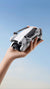 Hand holding a compact drone against a clear blue sky