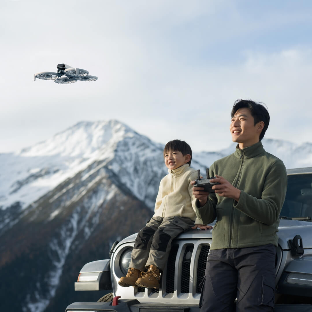 DJI Flip drone flying above man and child sitting on car hood in mountain landscape