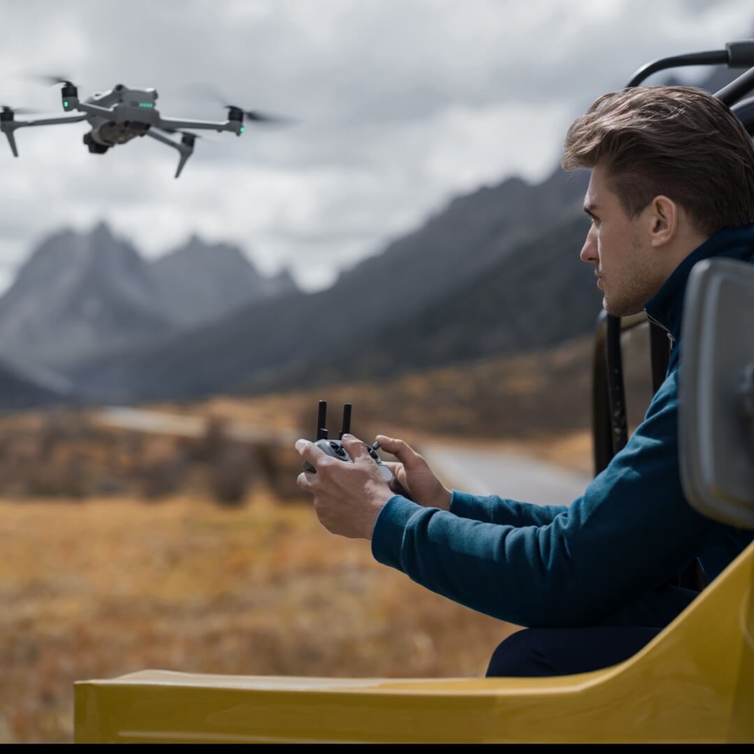 Man operating a drone in a scenic outdoor setting with mountains and grasslands